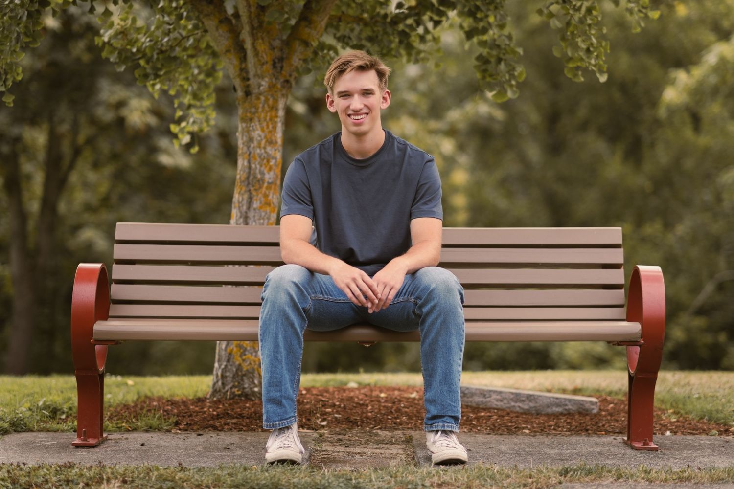 Senior boy sitting on park bench shoulders square to camera sitting and smiling