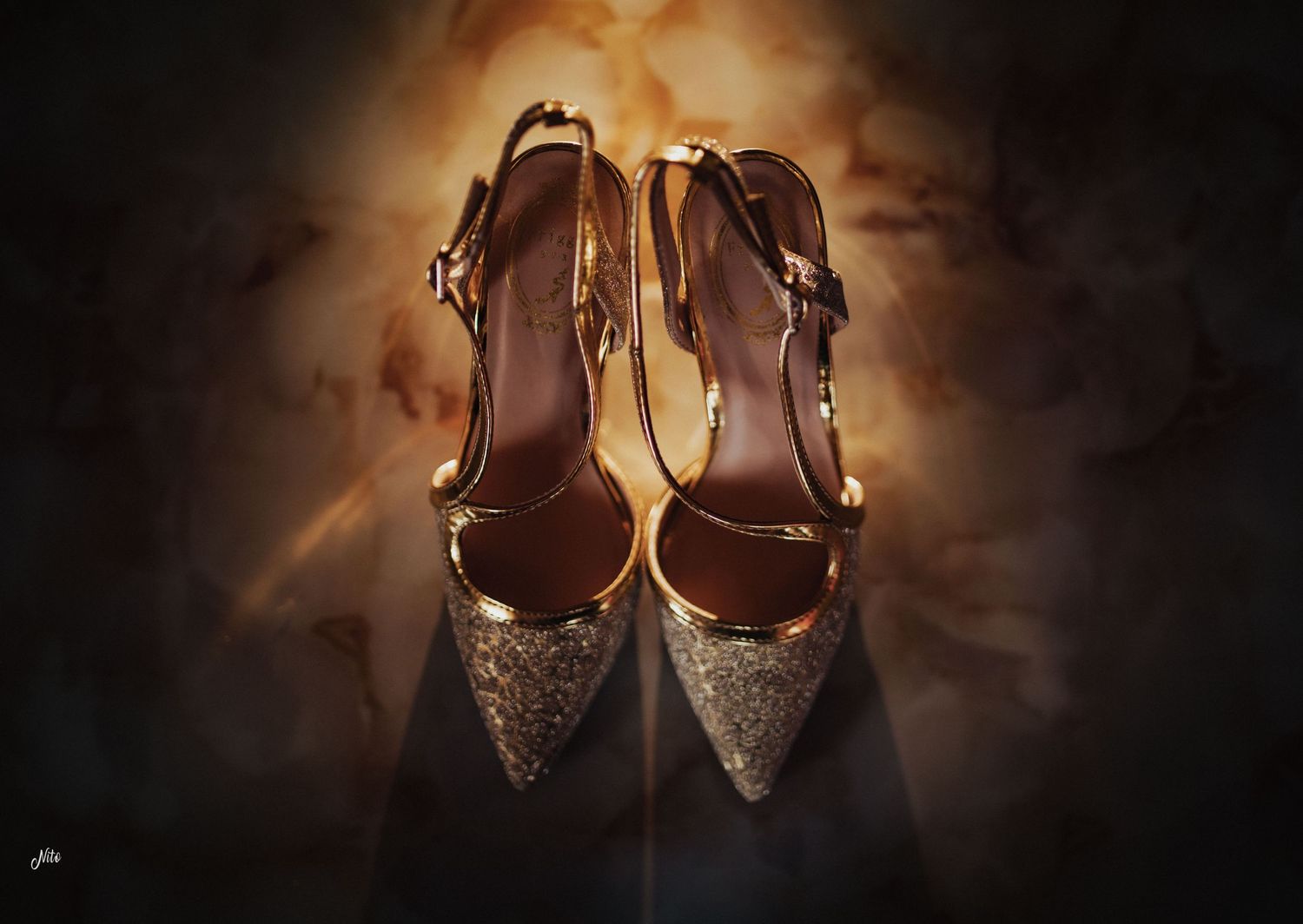 Glittery gold and brown wedding heels photographed against a warm illuminated background.