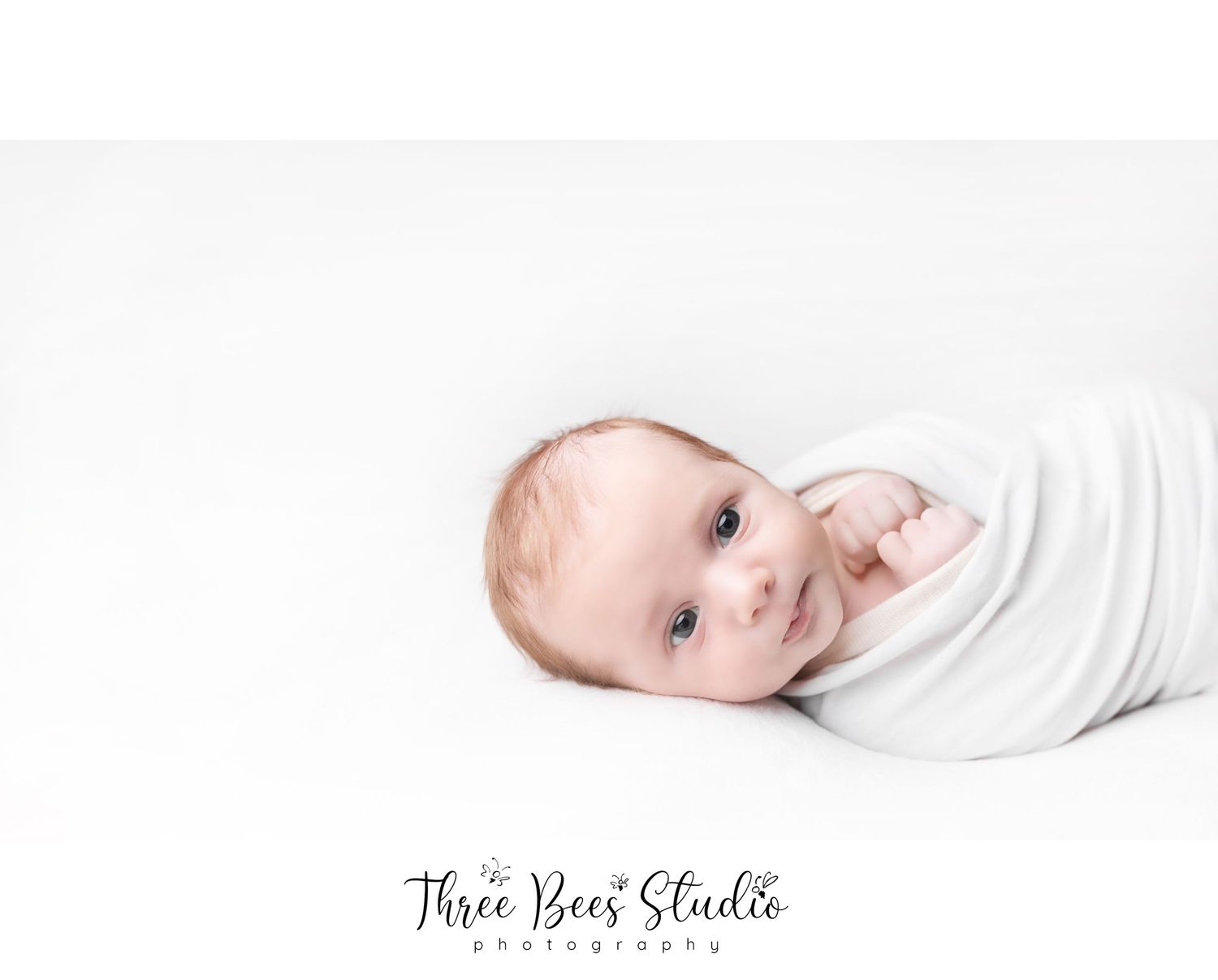 Baby swaddled in white fabric during minimalist photography session.