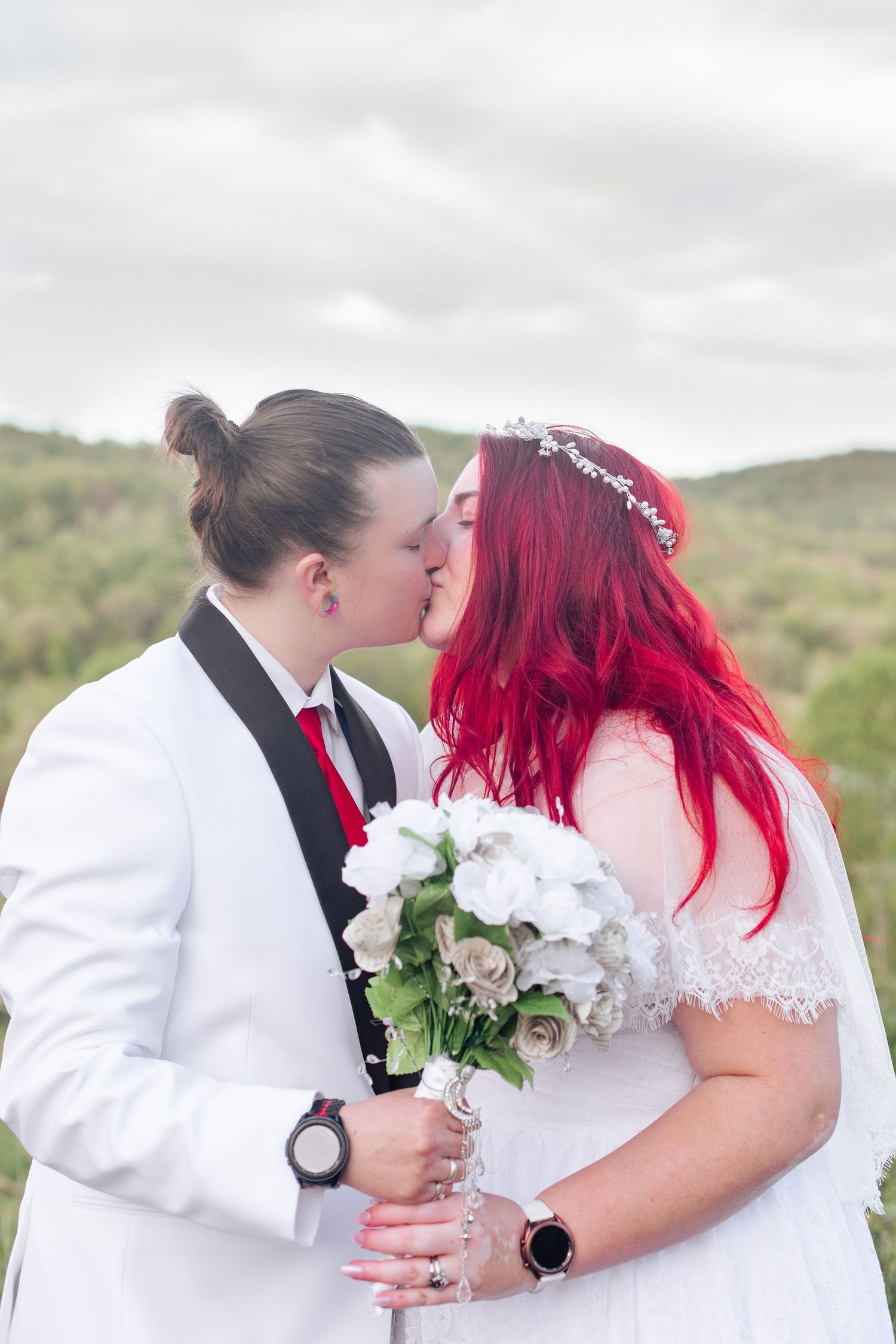 Newlyweds in white attire sharing a romantic moment with white roses against a natural backdrop.