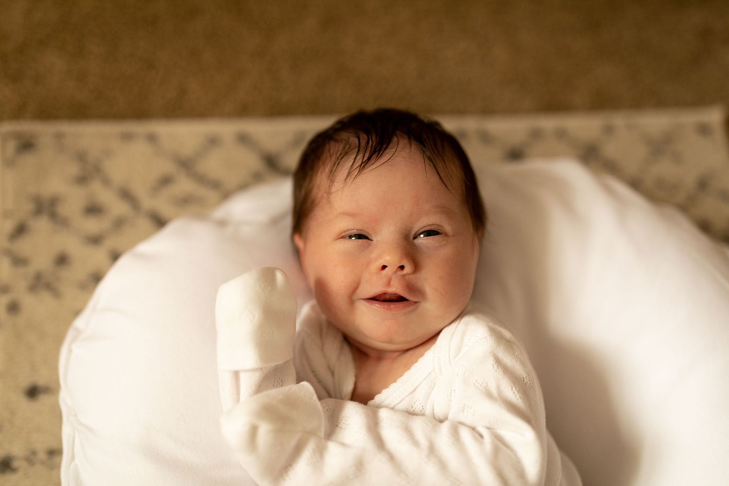 A peaceful infant wearing soft white clothing rests against plush bedding.