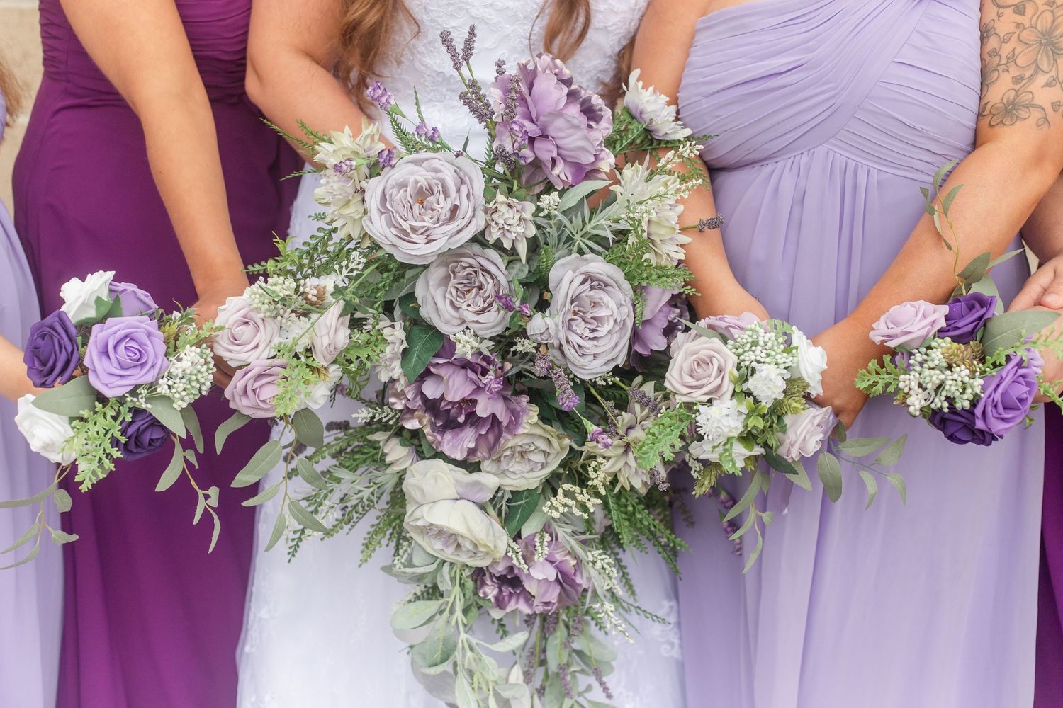 Bridesmaids hold purple and white floral bouquets against lavender dresses.