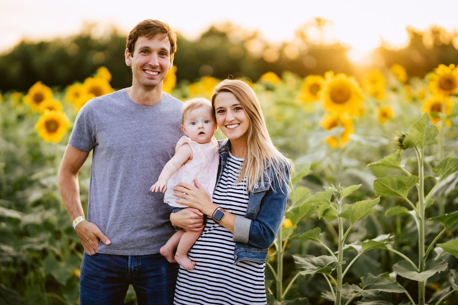 A family of three smiling in front of a field of sunflowers