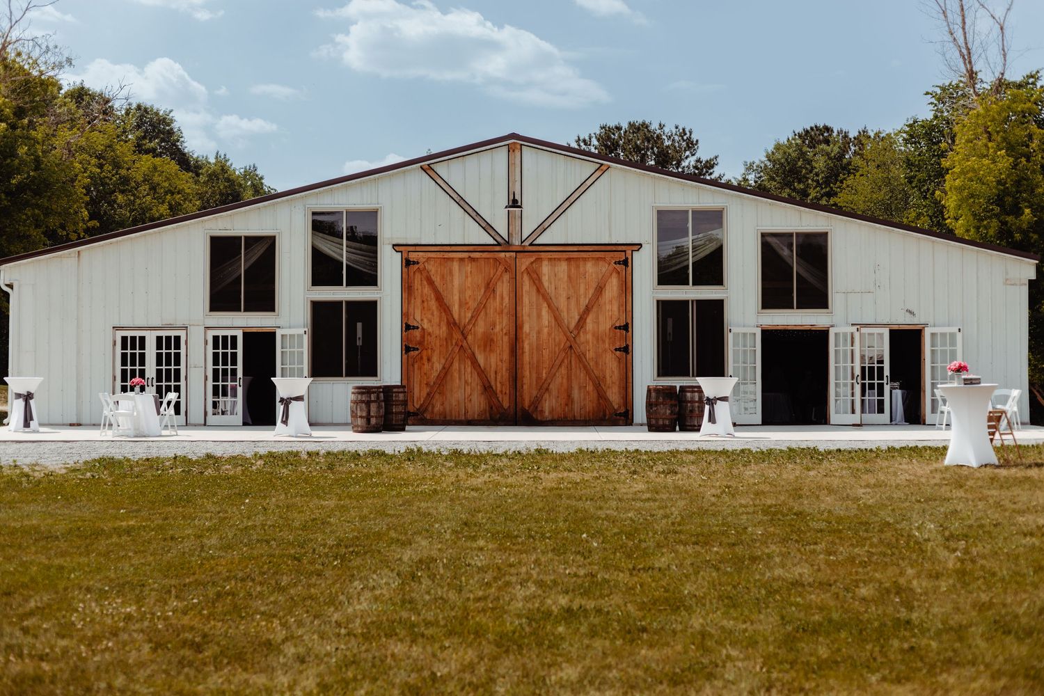 A modern white barn wedding venue with large wooden doors and windows on a sunny day.