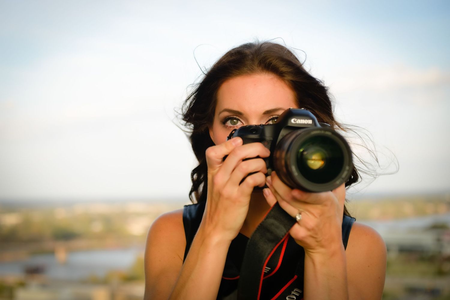 Beautiful woman holds camera up facing the viewer and only slightly looking over the camera. River background.