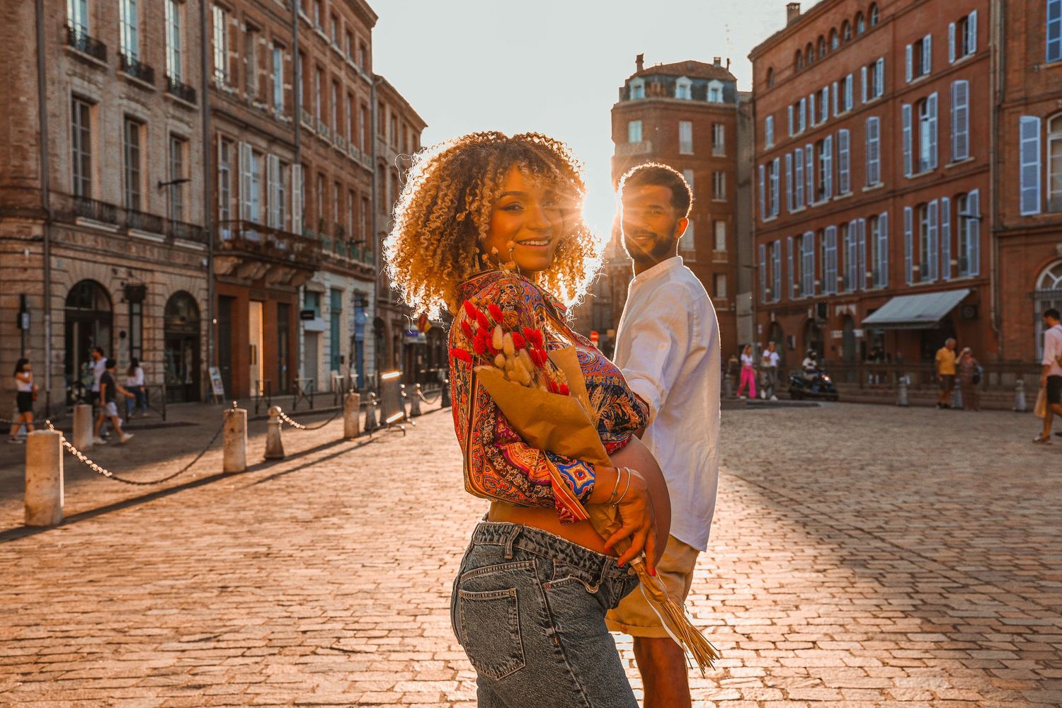 Couple dancing on cobblestone street at sunset with historic buildings in background.