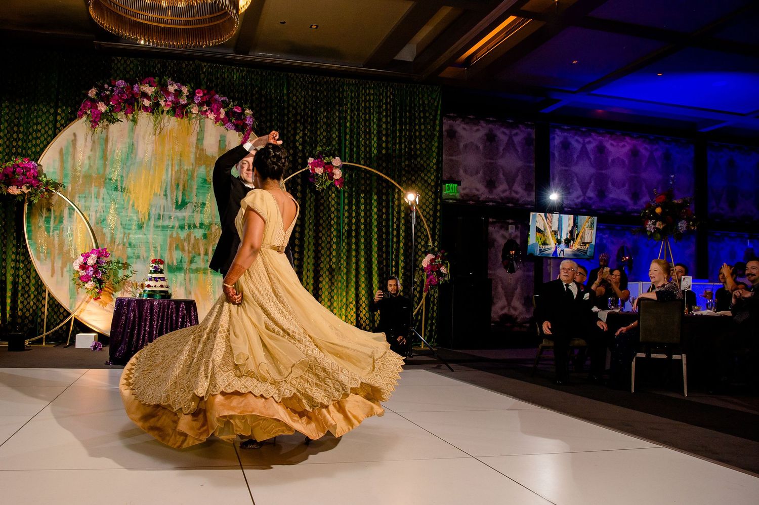 A flowing gold gown twirls gracefully on a white dance floor under decorative lighting.