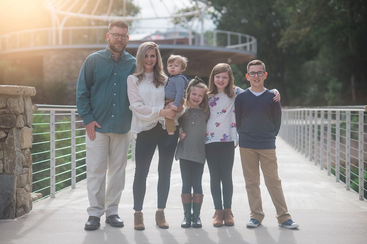 Family stands together on footbridge during sunset photoshoot.