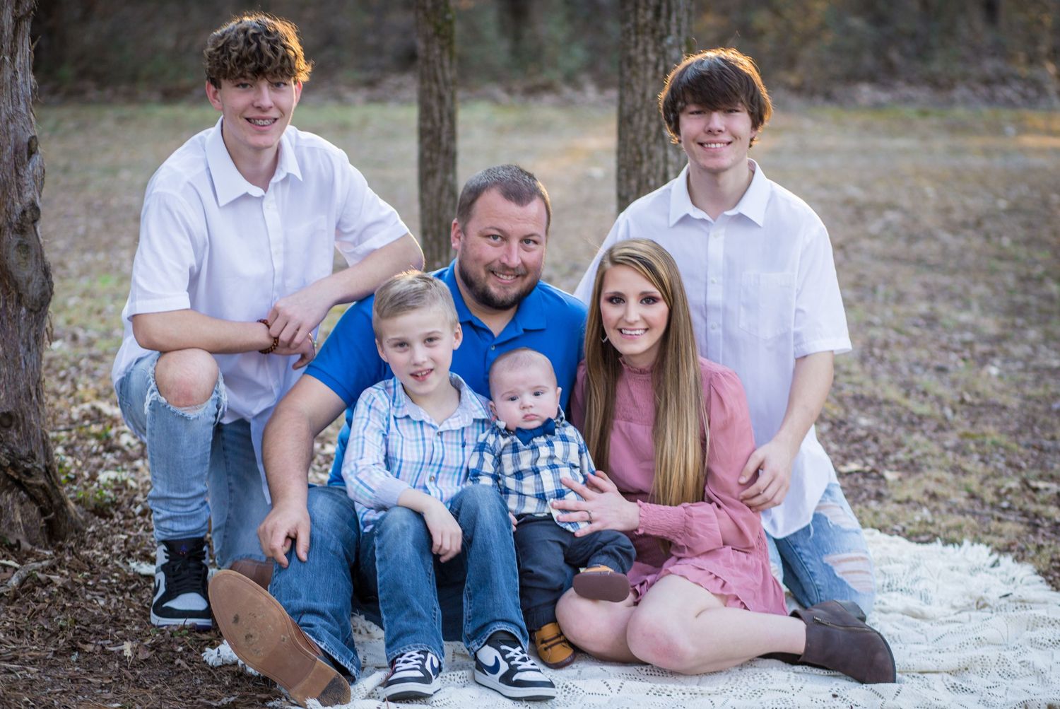 Family of six posing together outdoors in a wooded area for a portrait photo.