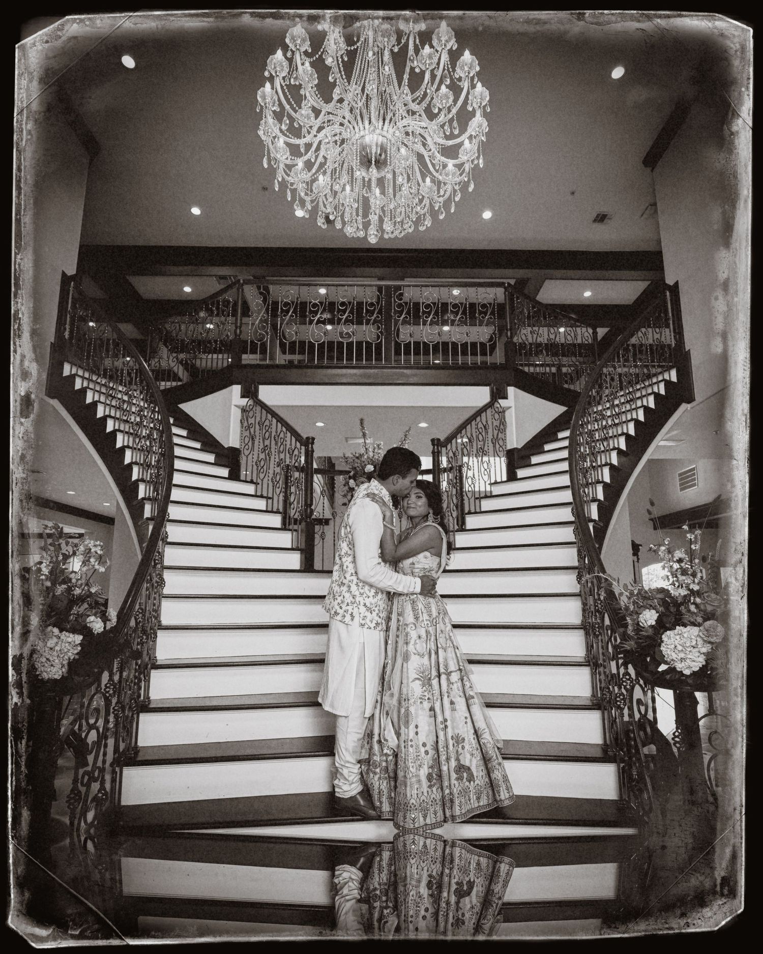 Romantic black and white photo on grand staircase under crystal chandelier.