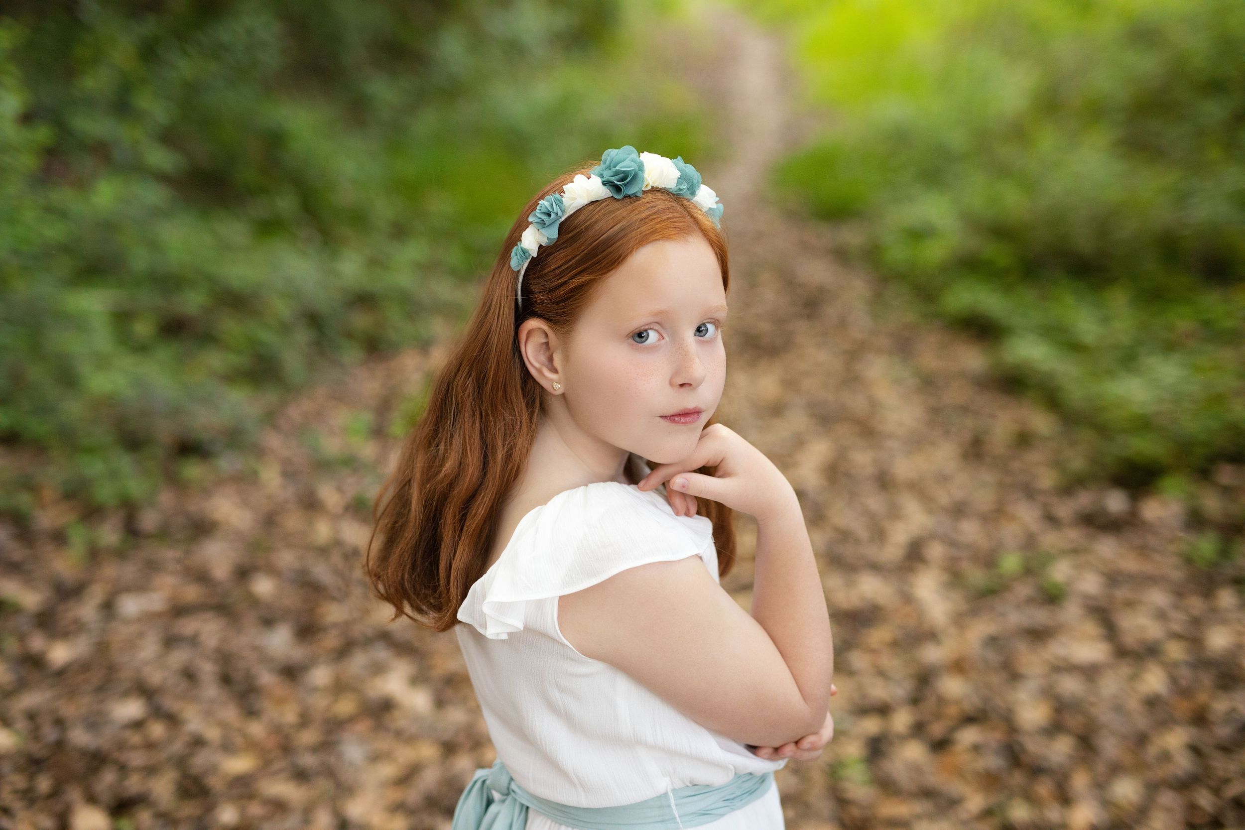 Portrait in nature wearing a white dress and floral headpiece on a wooded path.