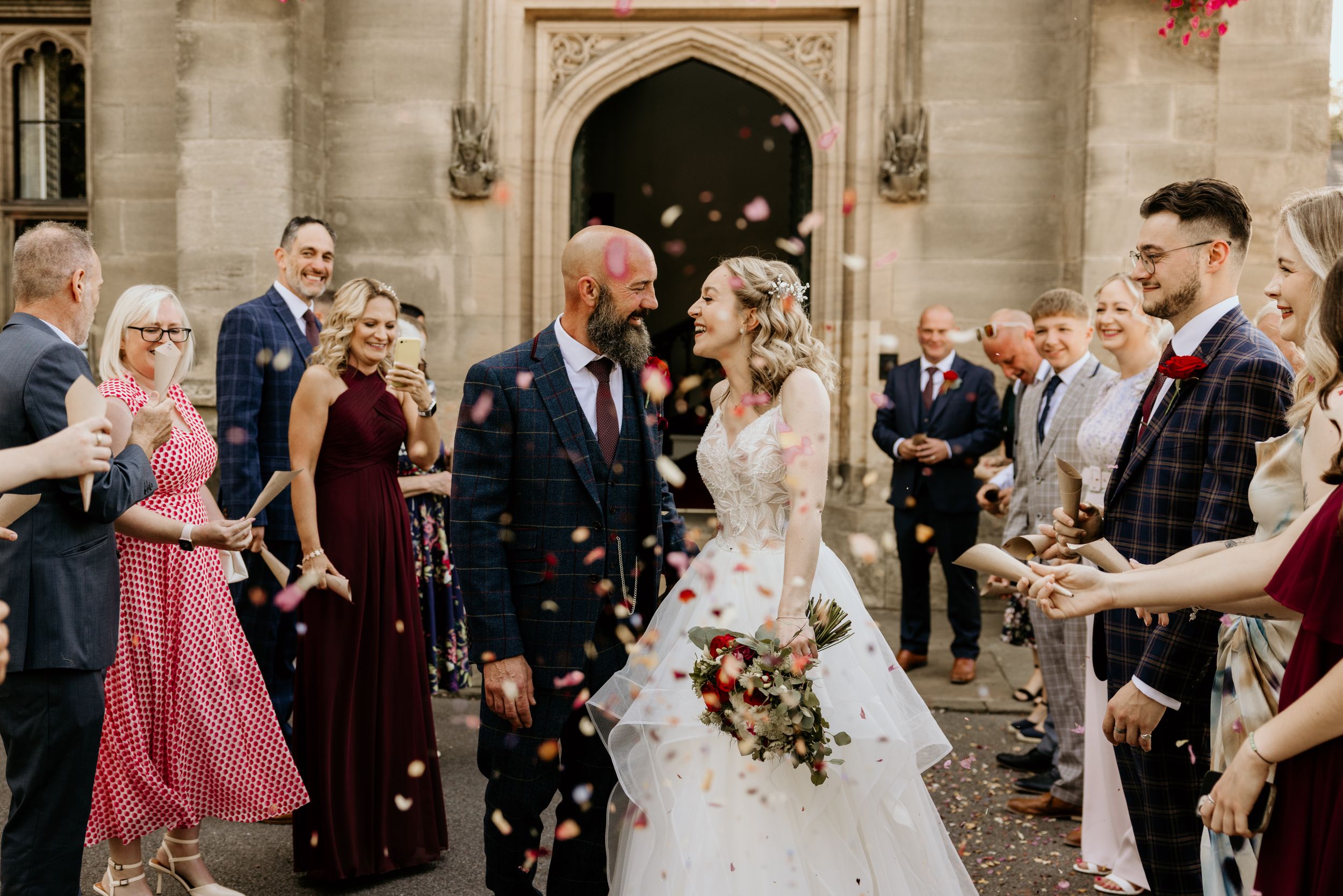 Joyful wedding ceremony moment with guests showering confetti on couple outside historic stone church entrance.