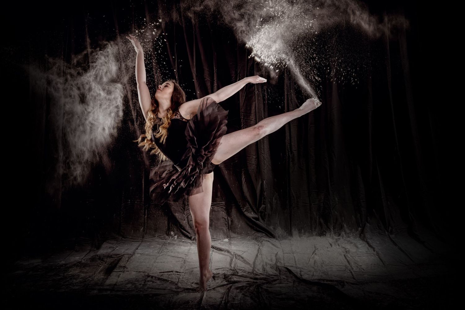 Dramatic dance pose with powder effect against dark background.