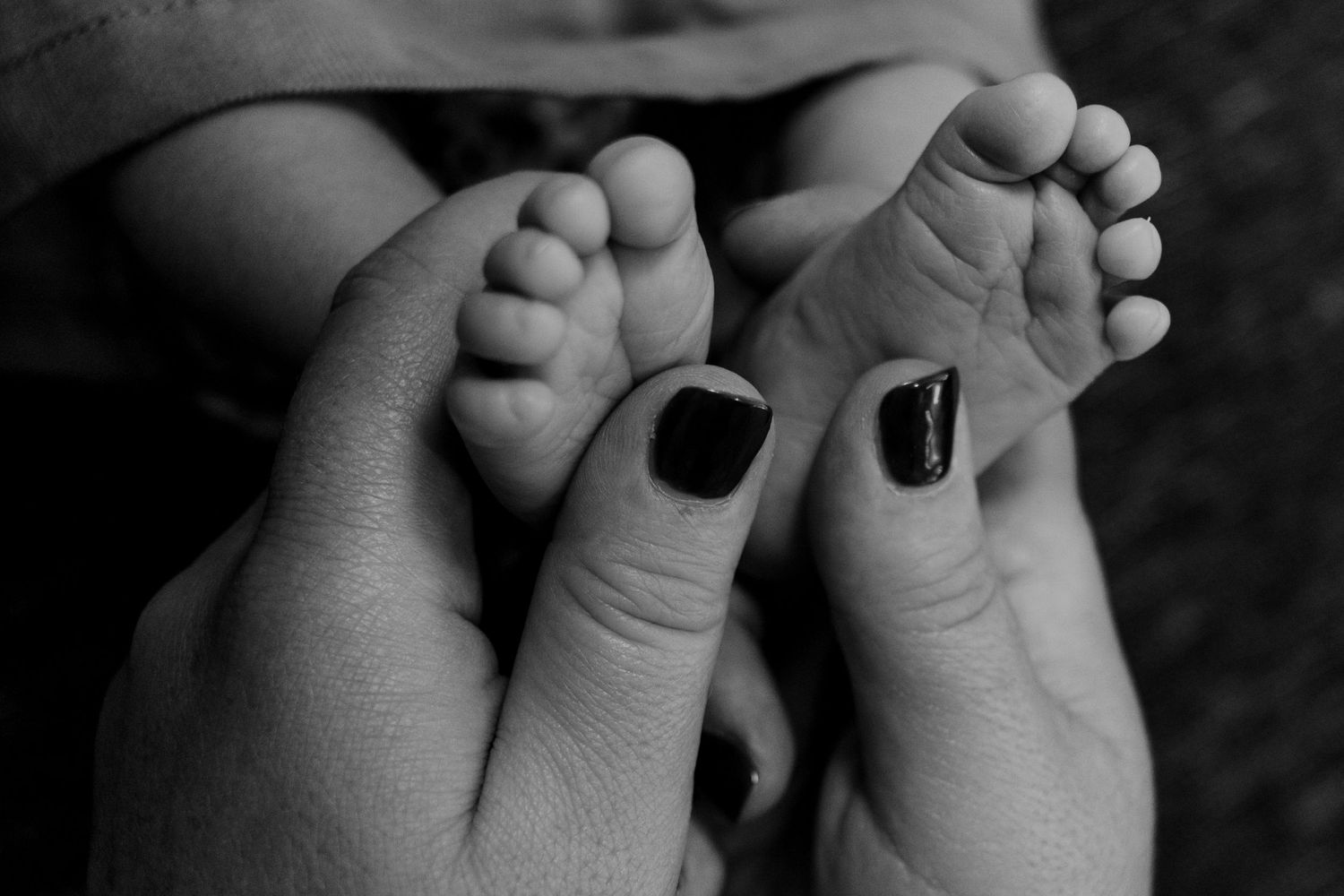 Black and white close-up of baby feet with painted toenails being held by adult hands.