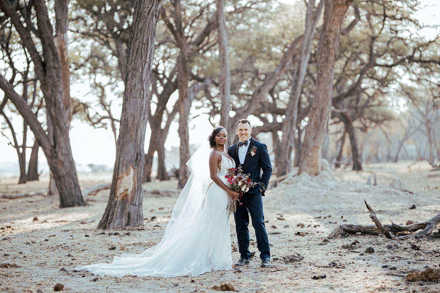 A couple in wedding attire standing among tall trees in a natural outdoor setting.