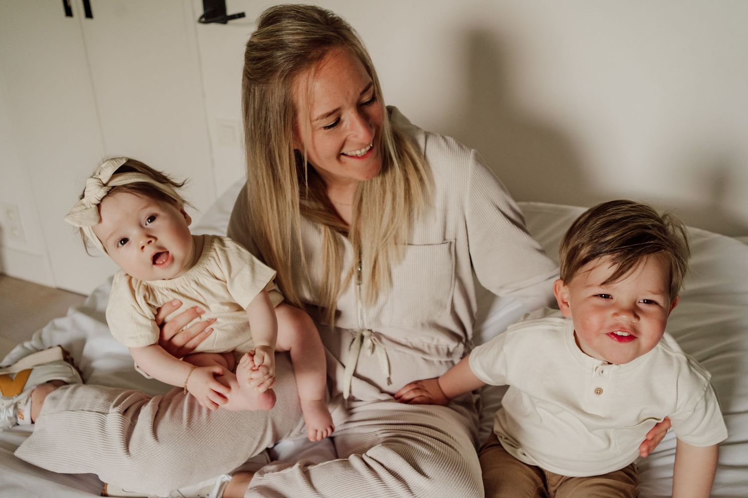 Mama op bed met dochtertje en zoontje, allen gekleed in beige kleding