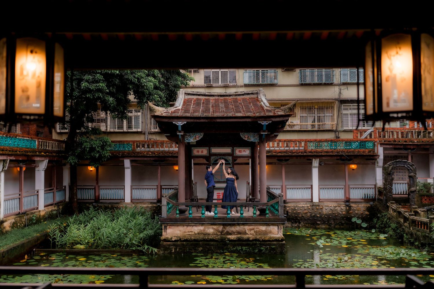 Couple embracing before a traditional Asian temple gazebo surrounded by lily ponds and lanterns at dusk at the Lin Family Mansion & Garden.