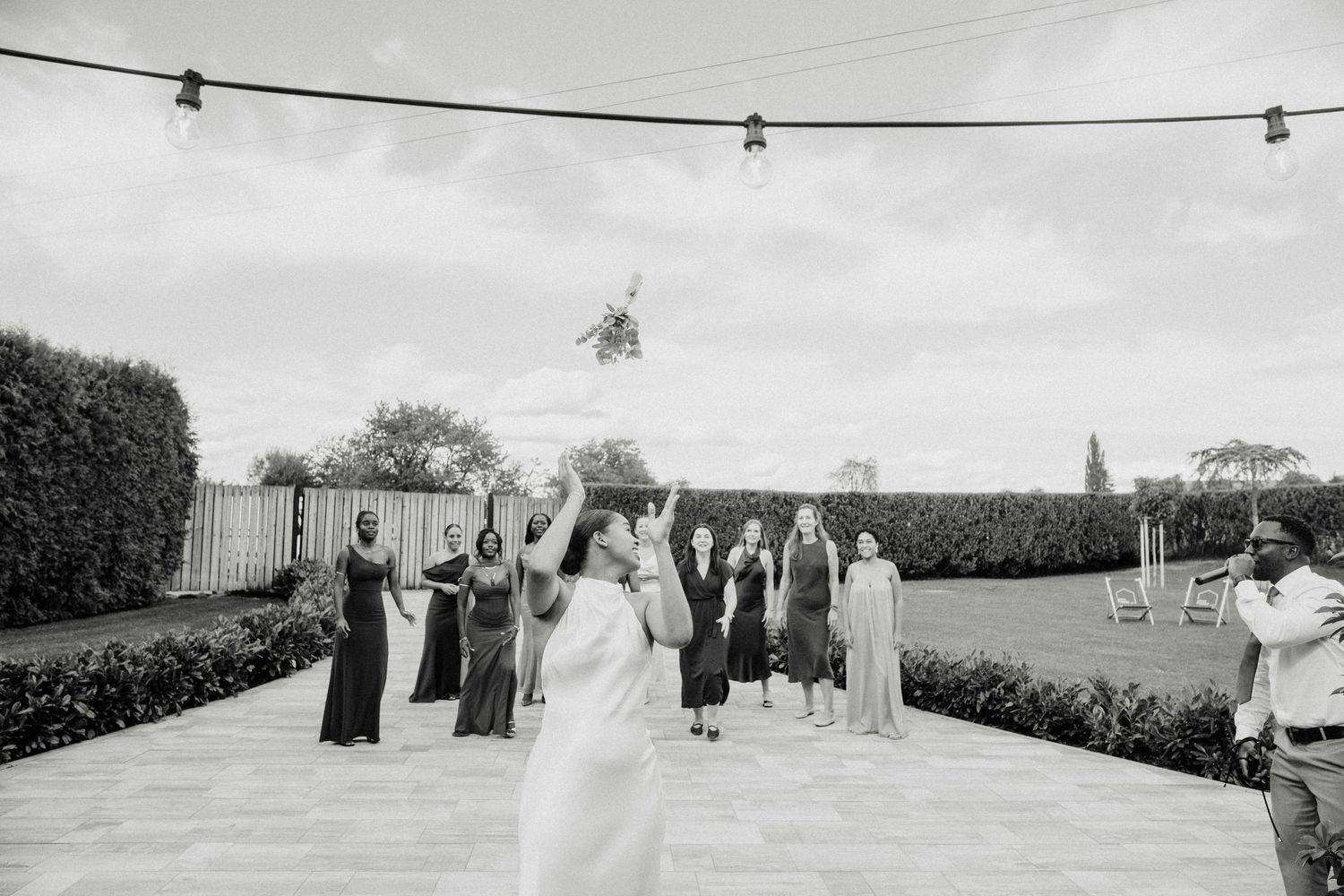 Bride tossing bouquet to bridesmaids outdoors at wedding reception in black and white photo.