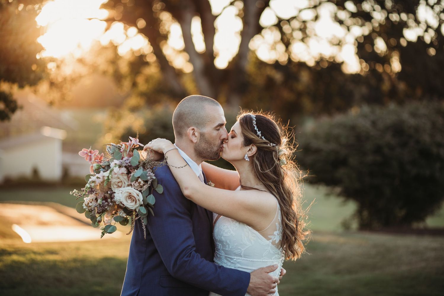 A couple embraces during golden hour sunset with a colorful bouquet of flowers.