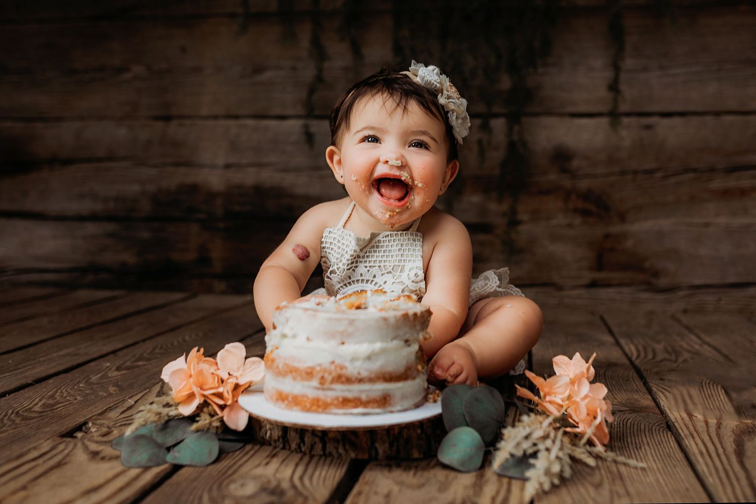 Baby's first birthday cake smash photography session on rustic wooden floor.