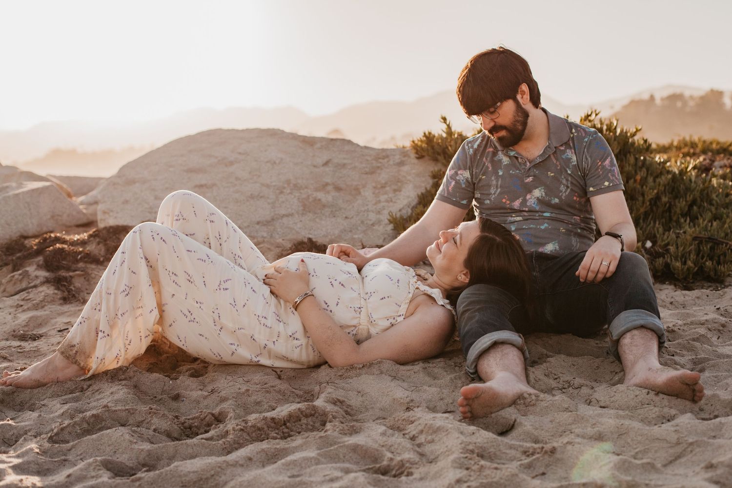 Couple lounging together on sandy beach during sunset photo session.