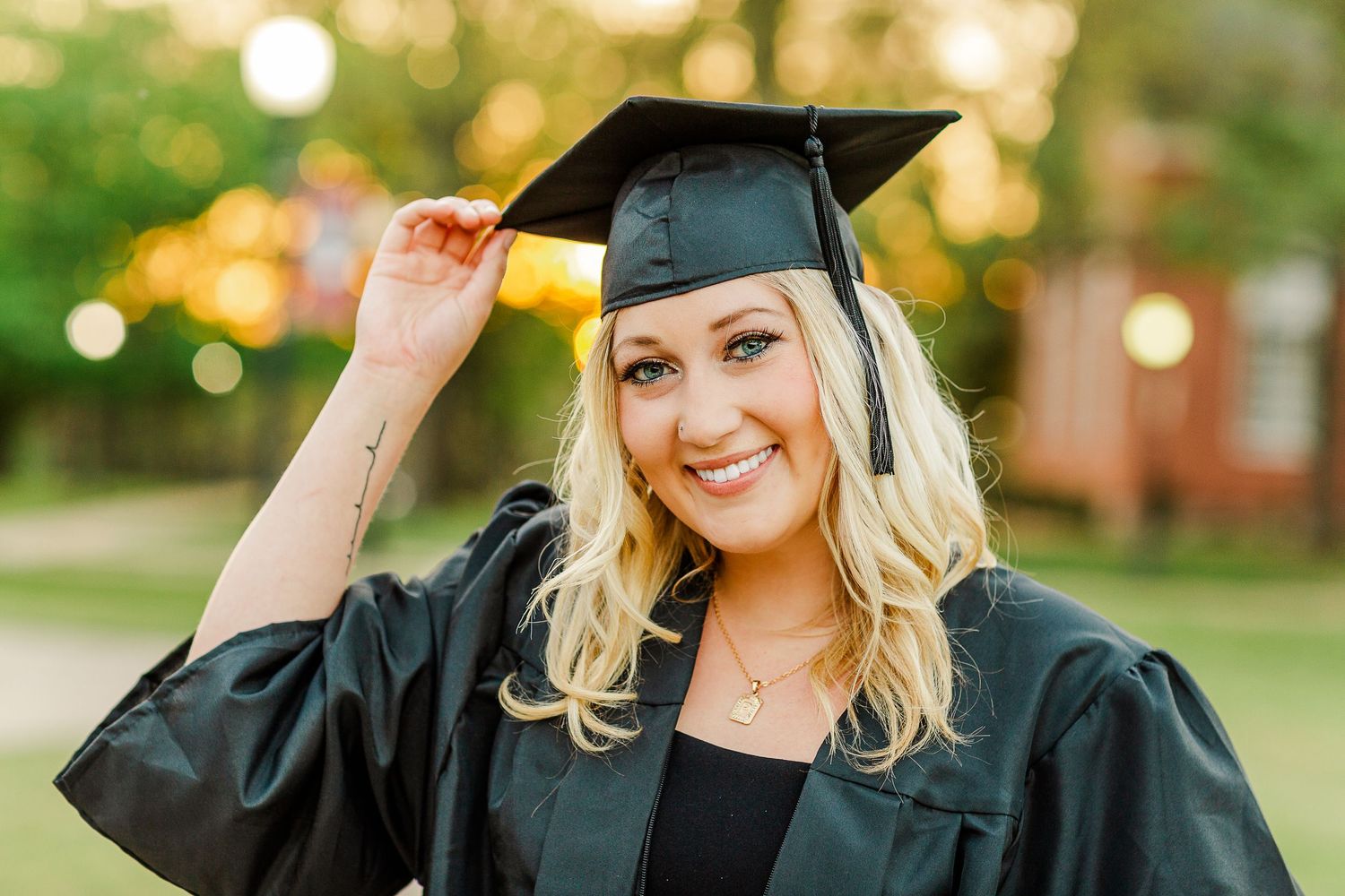 Graduate wearing traditional black cap and gown poses outdoors during golden hour.