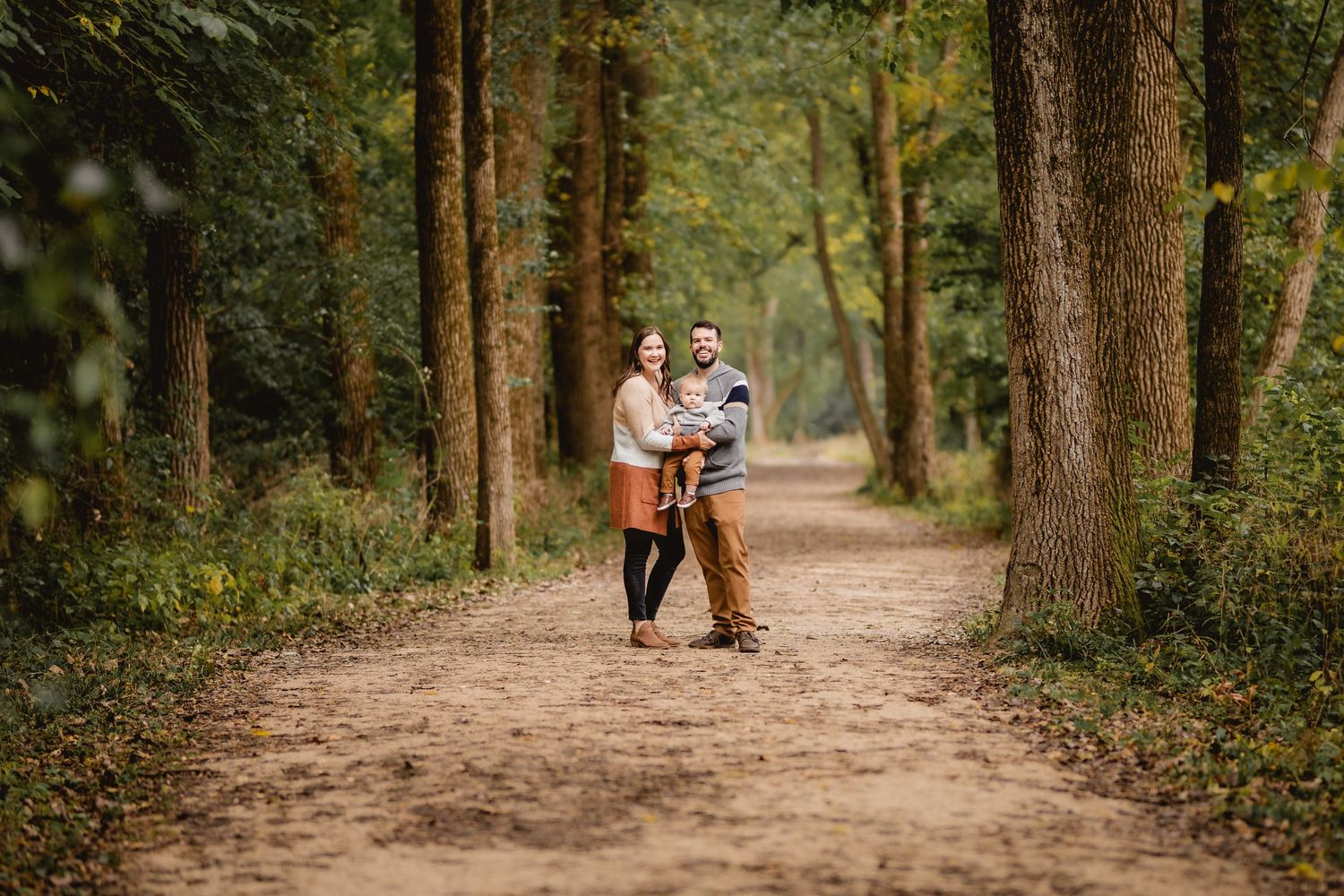 A family of three on a trail surrounded by tall trees