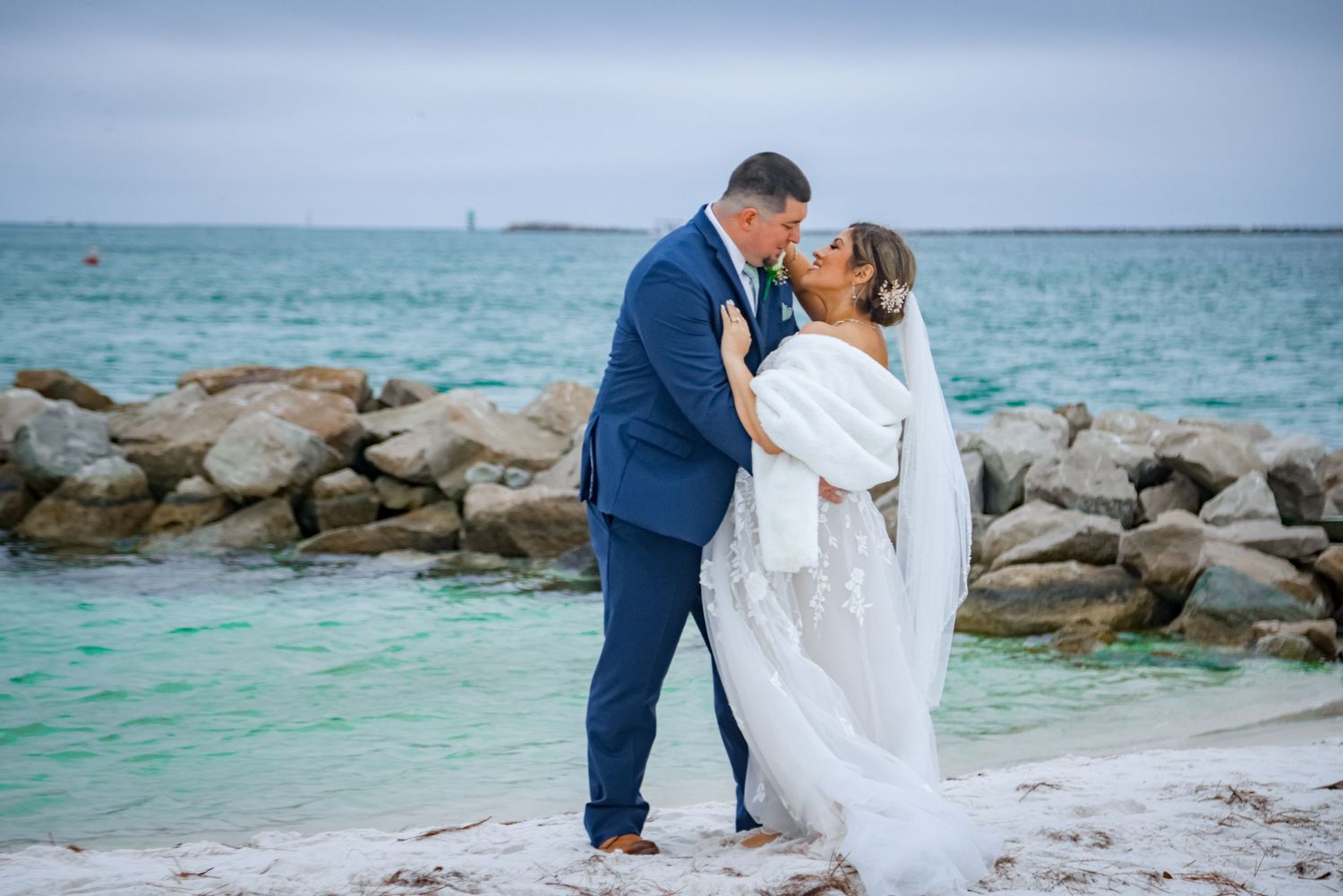 Romantic beach portrait with couple against turquoise ocean and rocky shore.