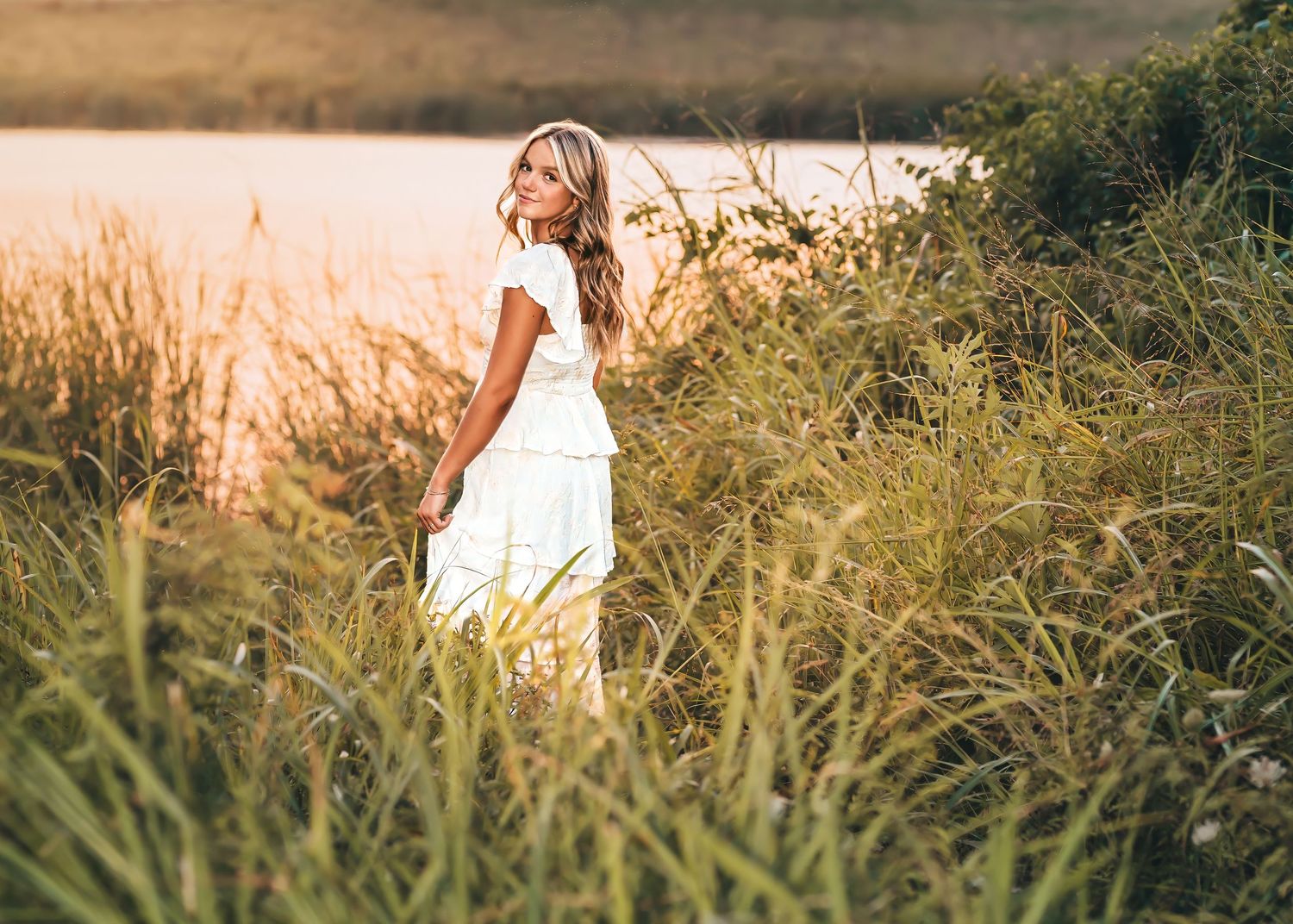 A white dress and cowboy boots create a rustic boho look against a golden sunset path in the countryside.