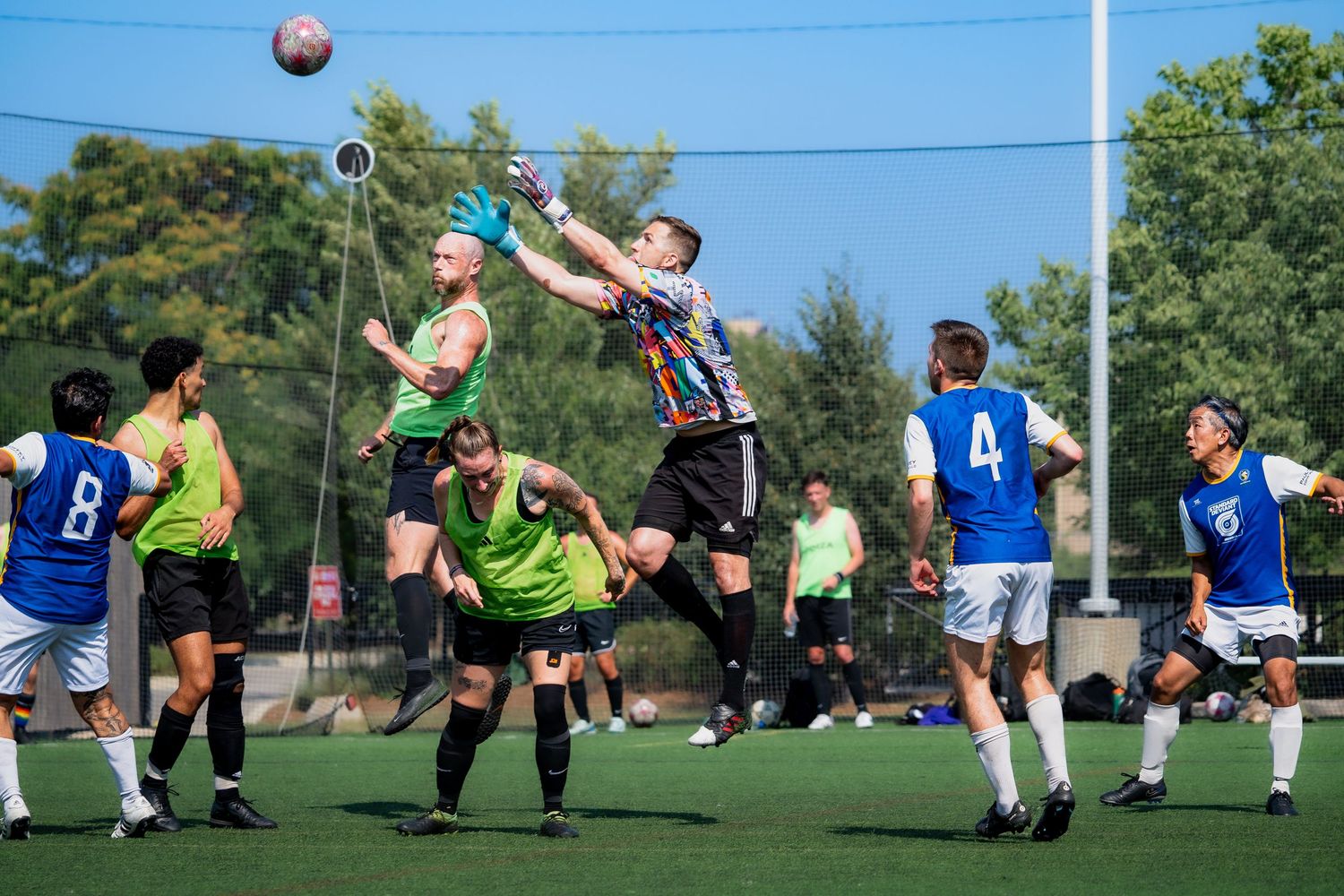 A soccer goalie jumps and reaches for an approaching ball over teammates and opponents