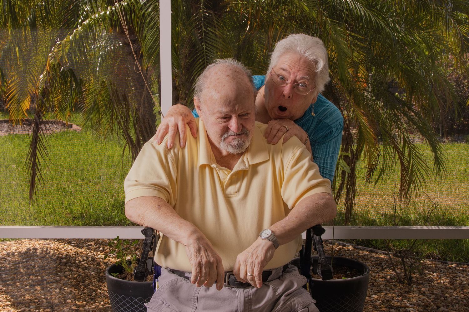 A caring moment shared between my parents on a covered patio with palm trees in the background.