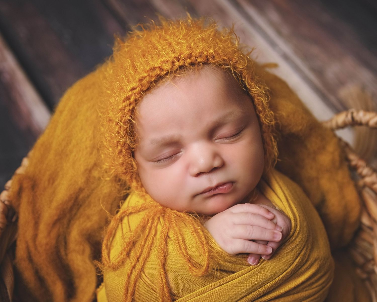 Sleeping newborn wrapped in golden yellow swaddle blanket with matching knit bonnet in professional studio portrait.