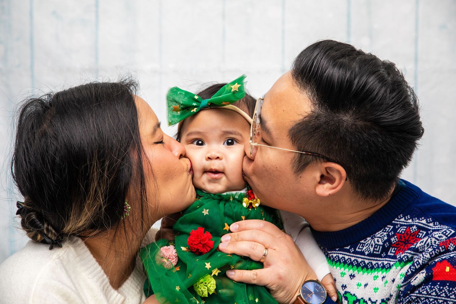 Parents share loving kisses with their baby wearing festive green holiday attire.