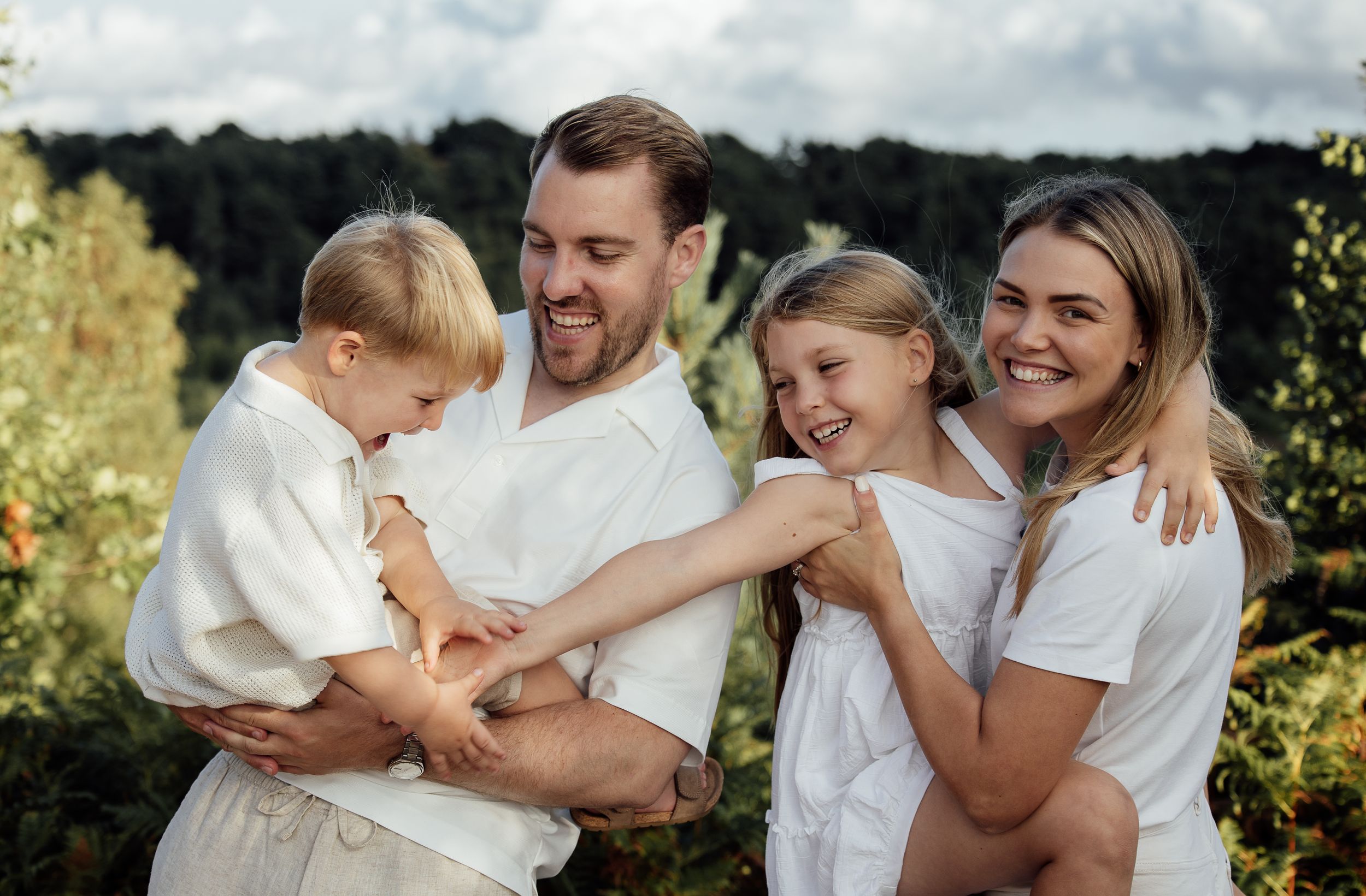 Fun natural family of four laughing together during a golden hour photo shoot.  Their clothes are styled to match in creams and whites.