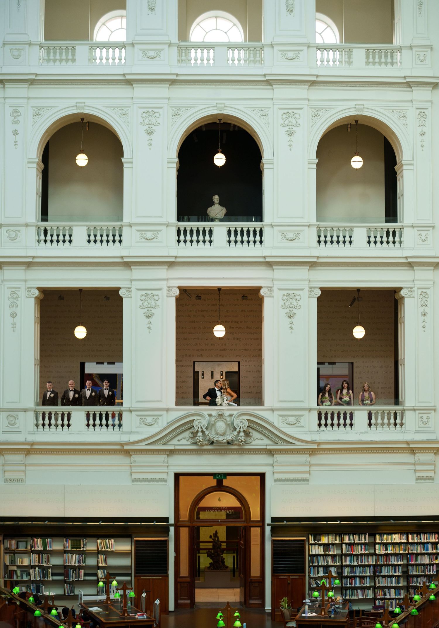 Elegant white arched interior of historic library with ornate balustrades, columns and built-in bookshelves illuminated by pendant lights.