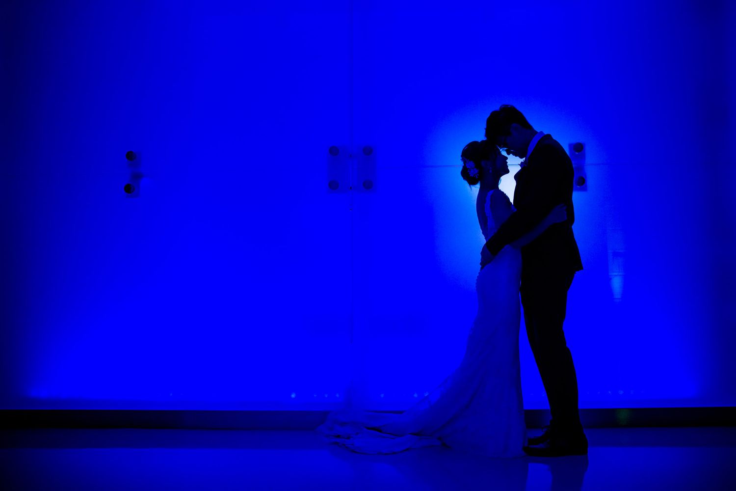 Silhouettes of a couple dancing in a romantic pose against a vibrant blue backdrop.