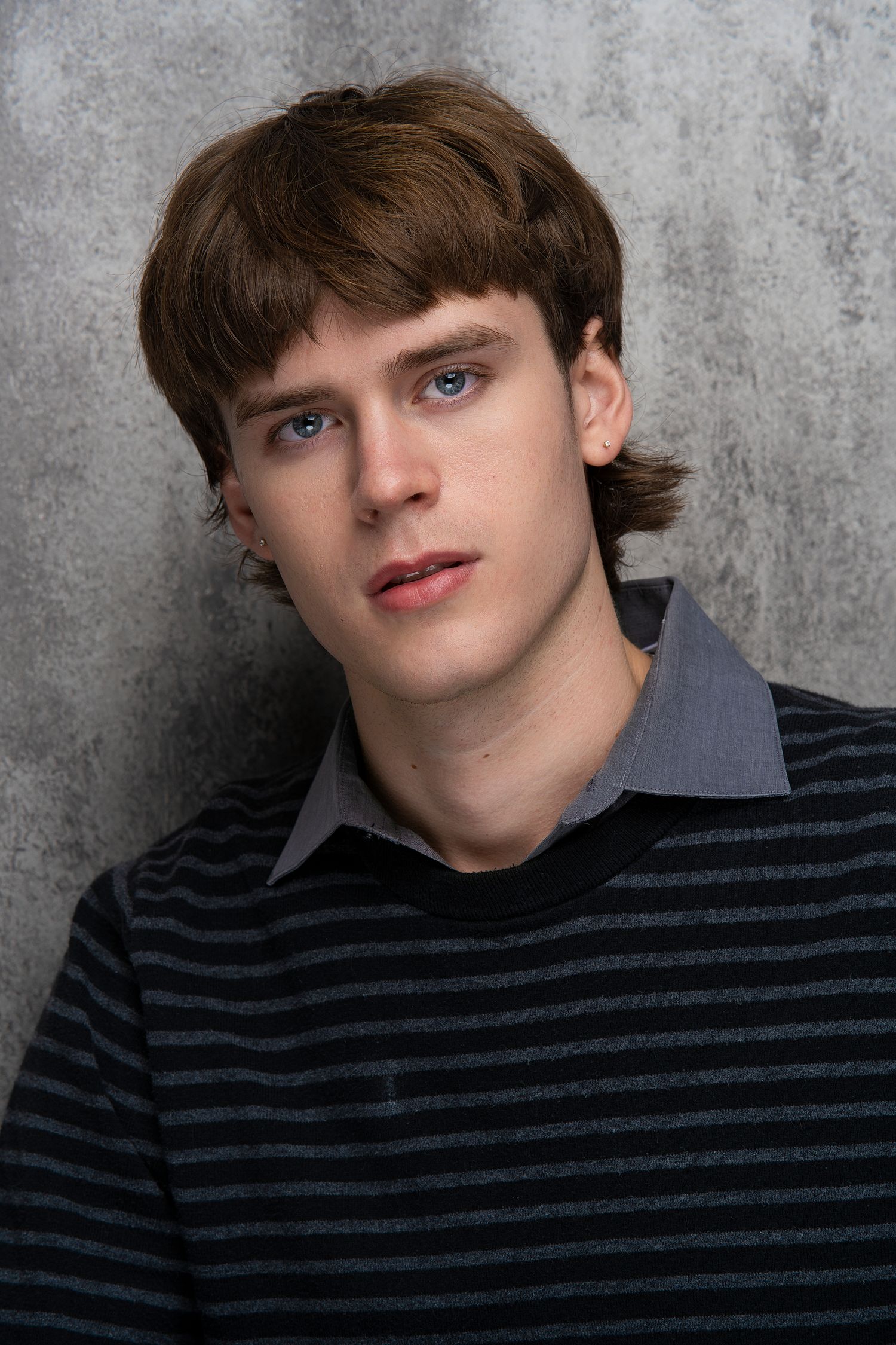 A person in a black striped sweater poses against a gray background in a series of similar headshots.