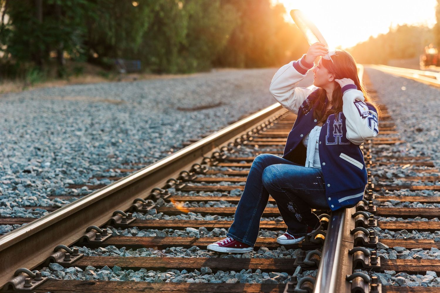 Person in casual wear sits on railroad tracks at sunset creating a moody silhouette against golden light.
