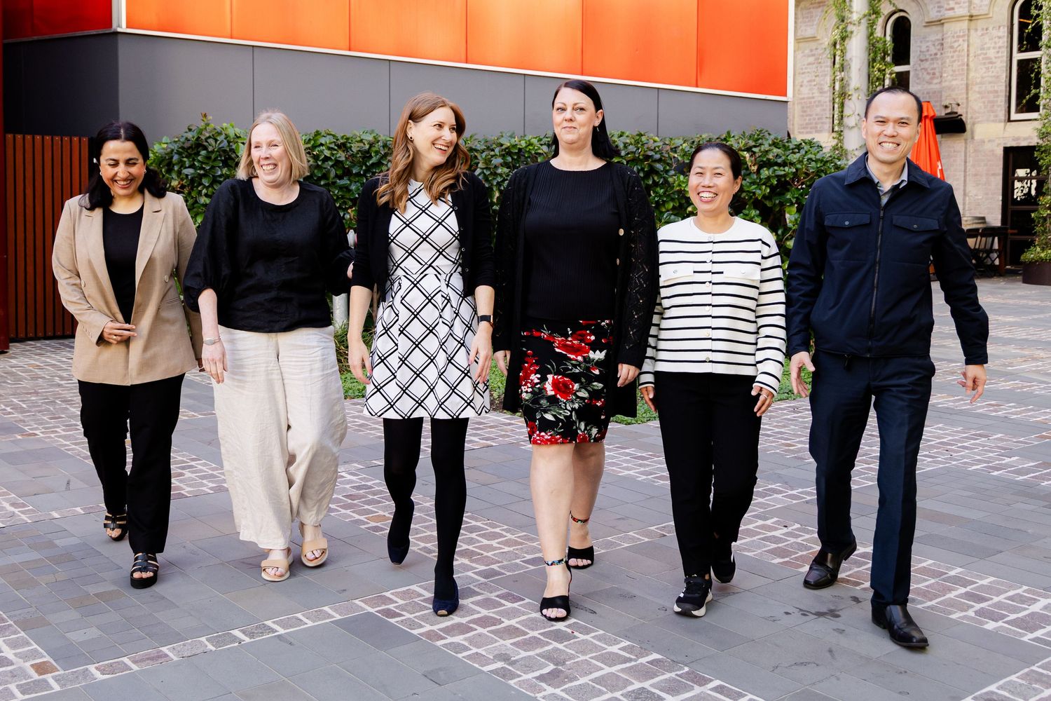 A group of coworkers walk together and smile while chatting in an outdoor courtyard area.