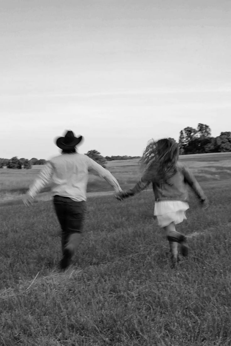 A couple holds hands while walking through a grassy field in black and white photography.