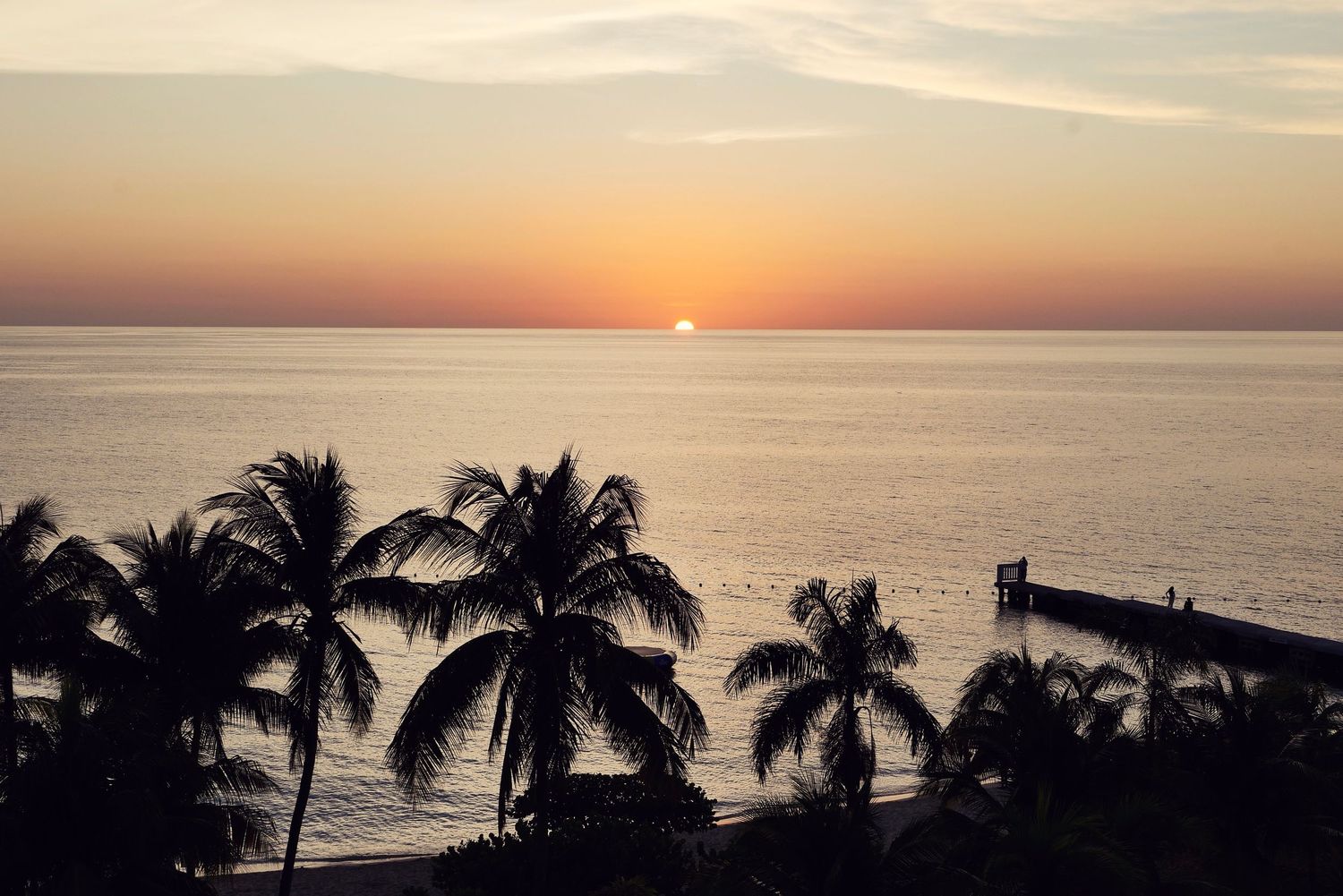 Luxurious beachfront resort with red lounge chairs and palm trees along swimming pool during golden sunset.