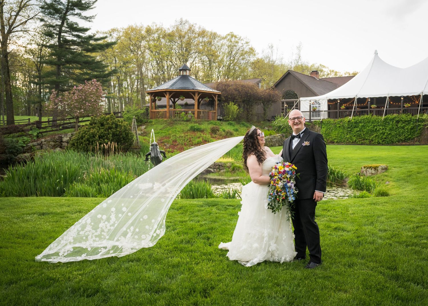 Newlyweds share an intimate moment outdoors with autumn foliage and rustic architecture in background.