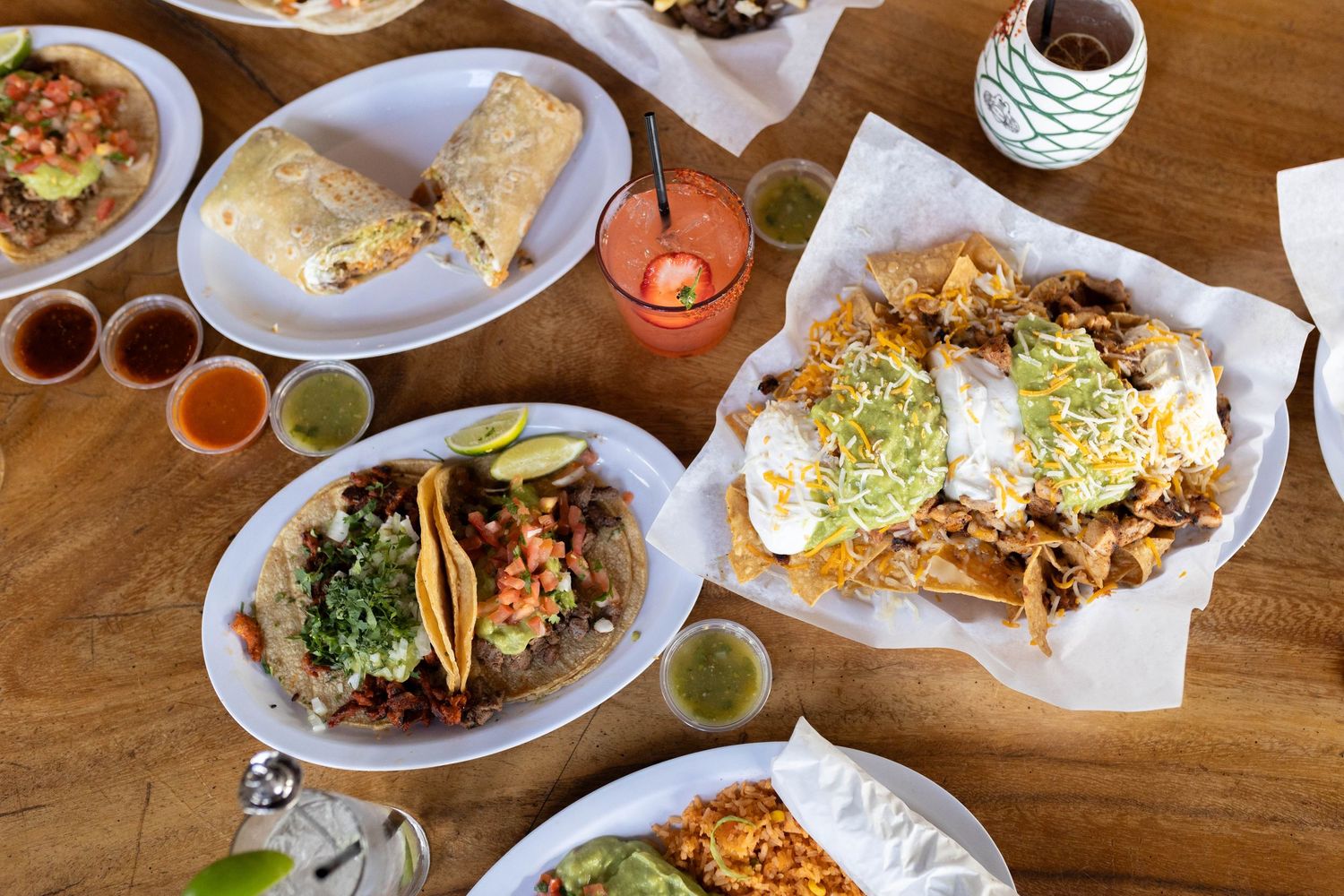 A close-up view of diverse dishes and beverages served on a wooden restaurant table during mealtime.