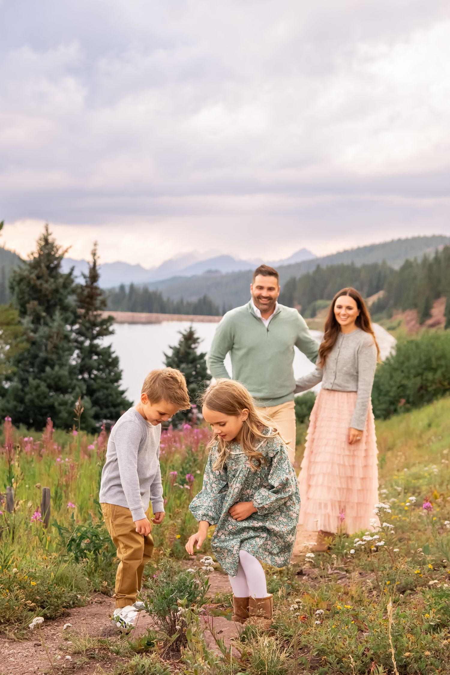 Family playing together in a wildflower meadow with mountains and lake in the background.