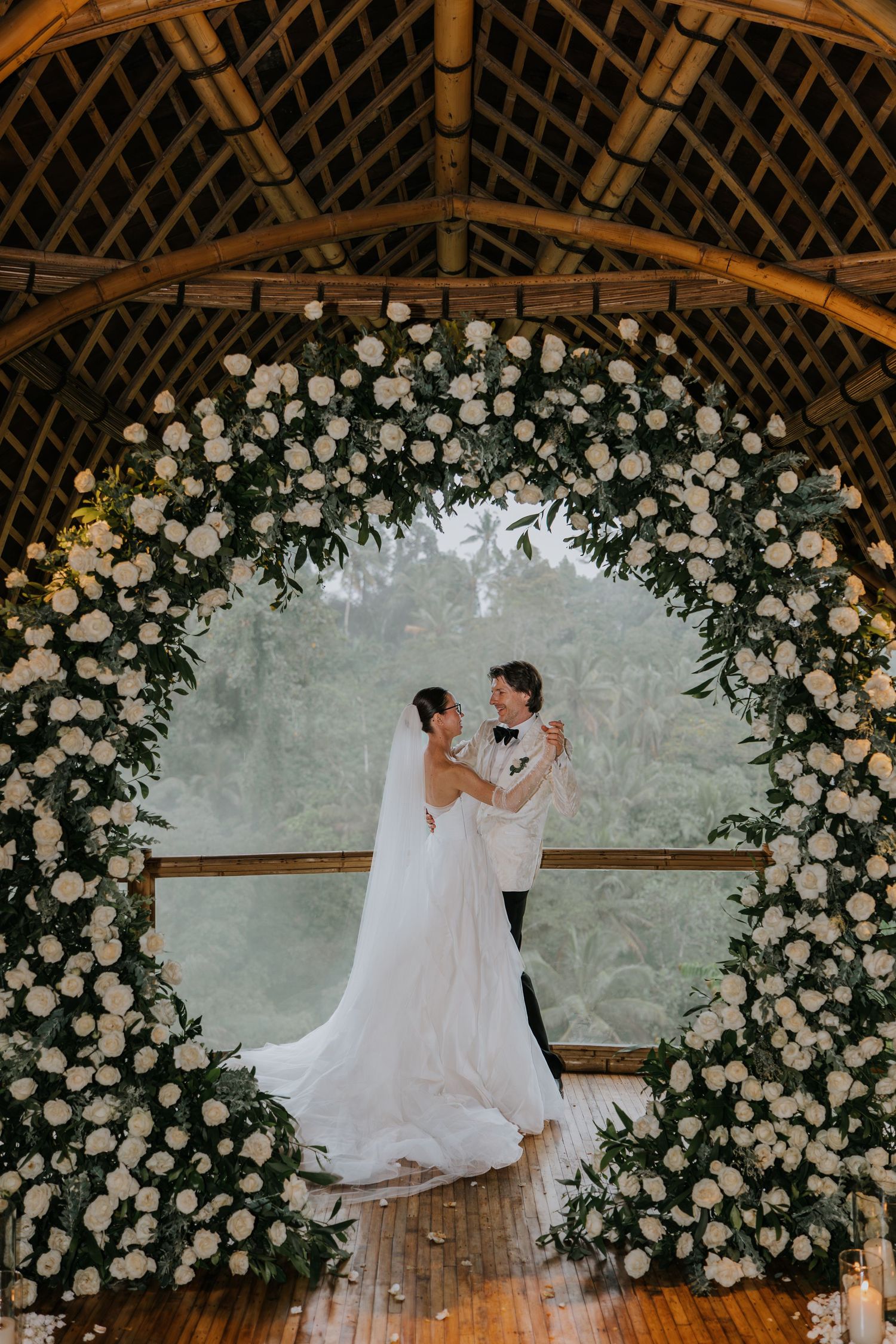 Elegant wedding arch adorned with white roses frames a romantic dance between newlyweds.