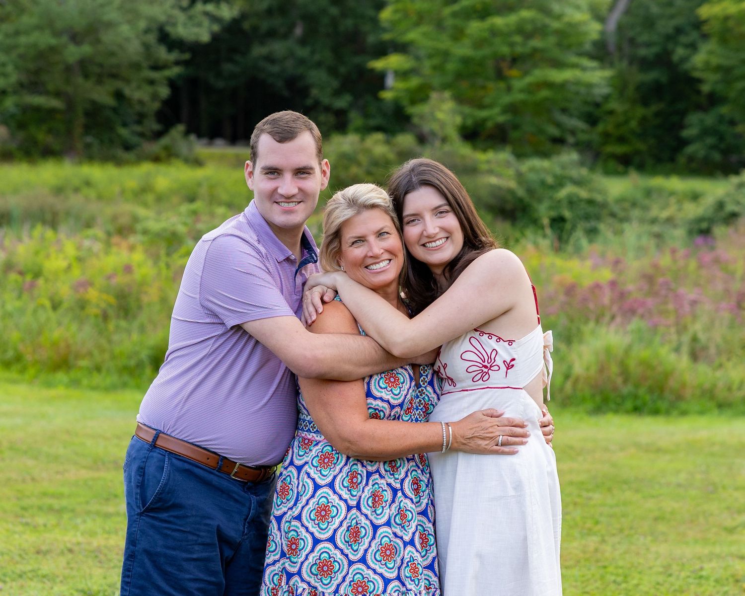 A family poses lovingly together outdoors in a grassy field with wildflowers in the background during a family photoshoot in Lincoln, MA.