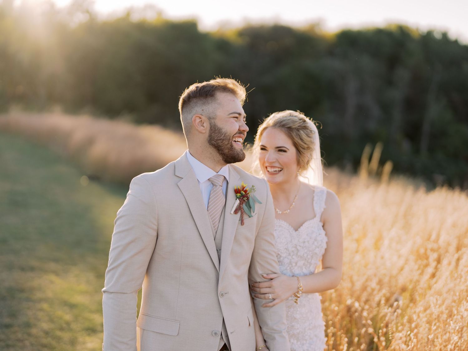 A wedding couple poses together outdoors, with the bride in a lace gown and groom wearing a yellow tie.