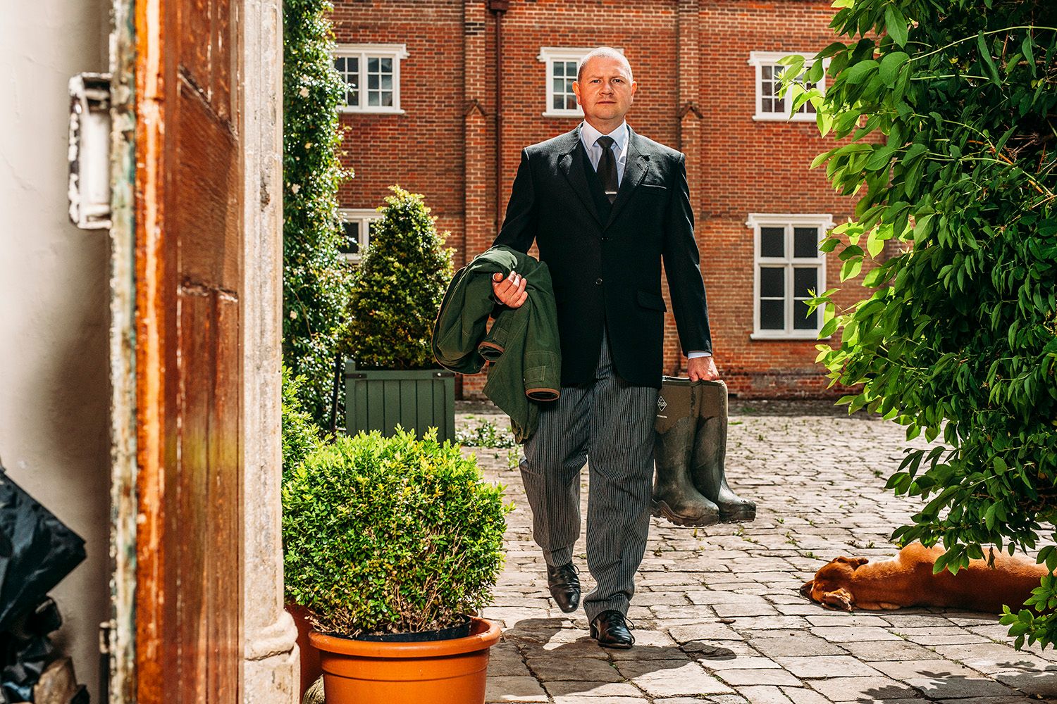 A figure walks through a stone-paved courtyard surrounded by red brick buildings and potted plants.