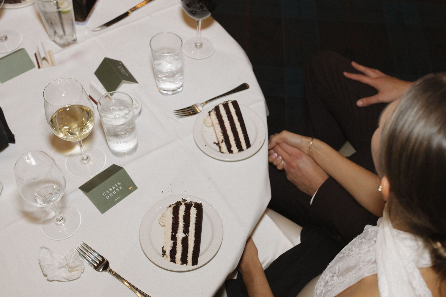 A row of elegant place settings at a formal dinner with white plates and wine glasses on a white tablecloth.