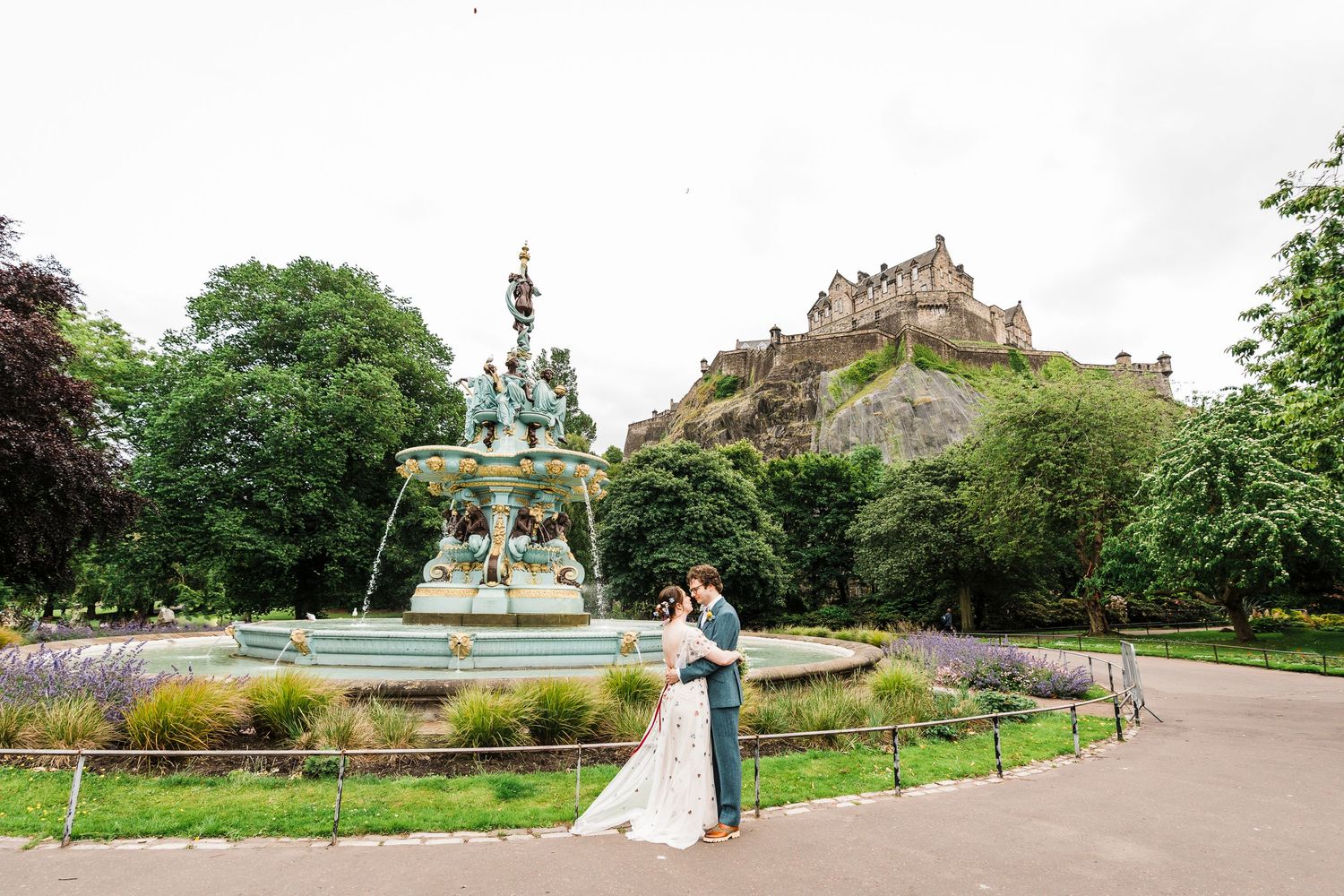 Wedding photograph at princes street garden fountain with castle in background. Bride an Groom hugging